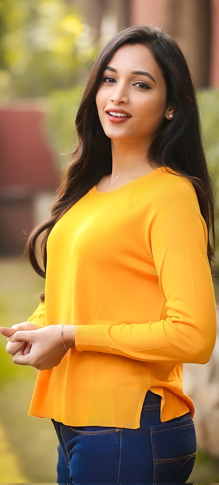 Srinidhi Shetty in a bright orange sweater and blue jeans with a warm outdoor smile HD phone wallpaper