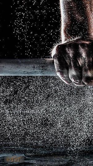 Gripping Hand on Weightlifting Bar with Flying Chalk Dust in Dark Gym HD phone wallpaper