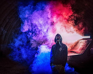 Person in Gas Mask and Hoodie Standing in Vibrant Blue and Red Smoke HD wallpaper