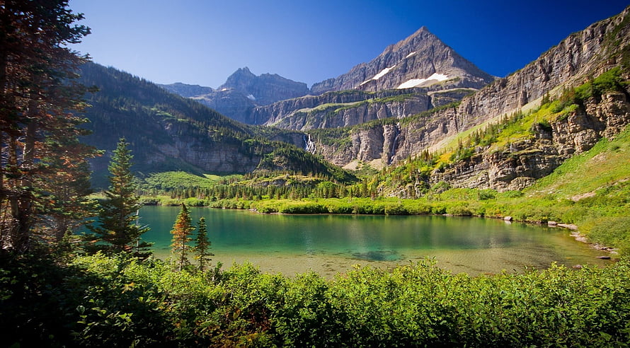 Alpine Lake Surrounded by Lush Green Forest and Rocky Mountain Peaks Under a Clear Blue Sky HD wallpaper