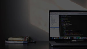 MacBook Pro on a desk displaying code editor with books and soft natural light HD wallpaper