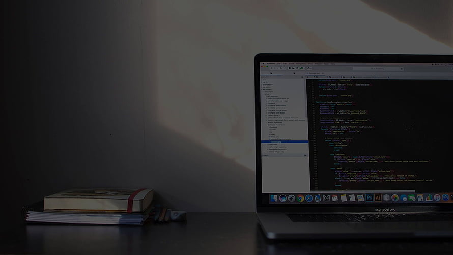 MacBook Pro on a desk displaying code editor with books and soft natural light HD wallpaper