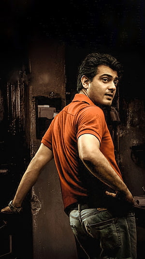Ajith Kumar in an orange polo shirt standing in a dimly lit urban alleyway HD phone wallpaper