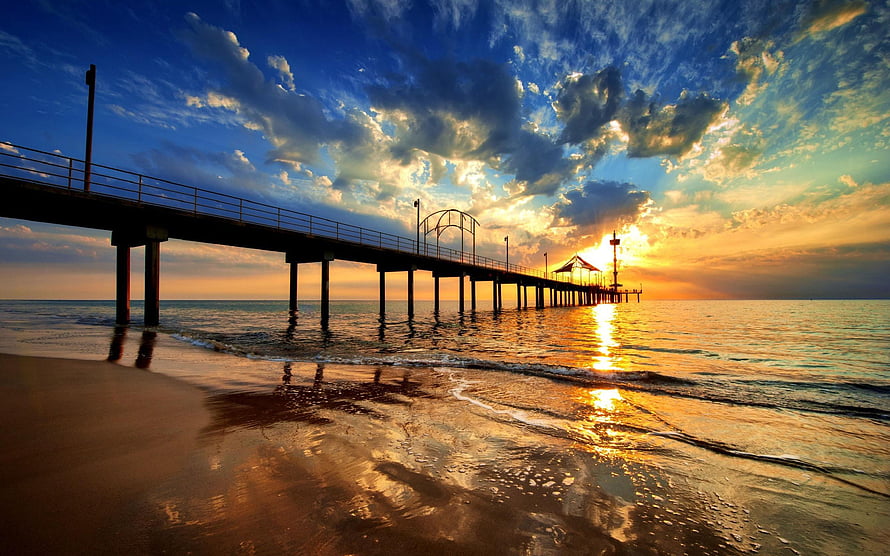 Golden sunset over a long pier extending into the calm ocean with dramatic clouds HD wallpaper