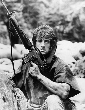 Sylvester Stallone as John Rambo in First Blood, holding an M60 machine gun in a black and white still HD phone wallpaper