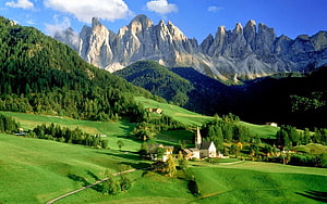 Alpine Village with Church Nestled in Green Meadows Beneath Dramatic Dolomite Peaks HD wallpaper