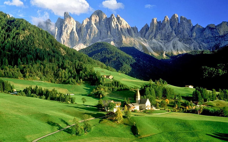 Alpine Village with Church Nestled in Green Meadows Beneath Dramatic Dolomite Peaks HD wallpaper