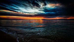 Dramatic Ocean Sunset with Fiery Horizon and Dark Stormy Clouds HD wallpaper