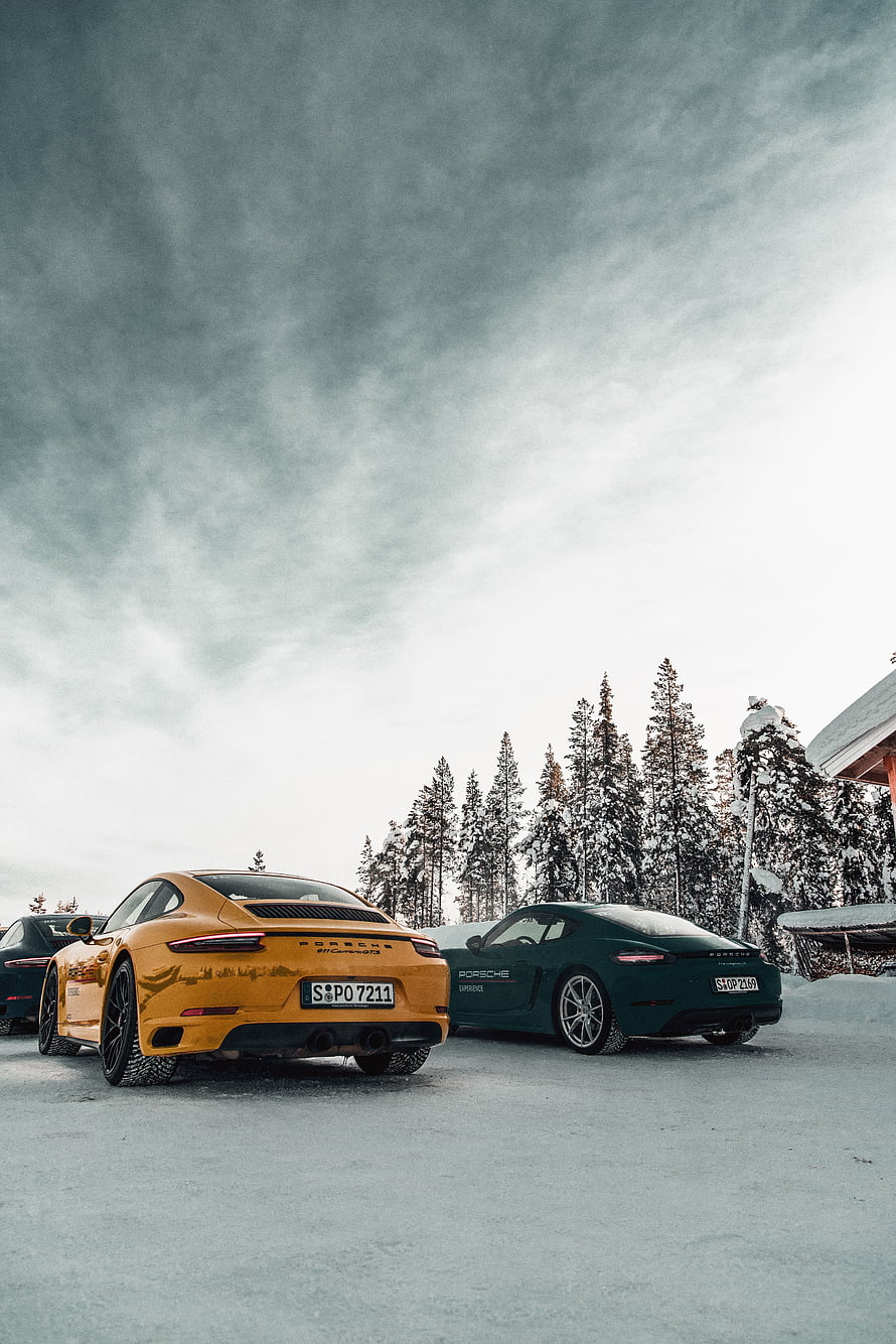 Porsche 911 and Cayman parked on snow-covered ground under overcast winter sky HD phone wallpaper