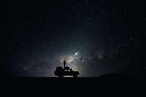 Silhouette of a person standing on a vehicle beneath the Milky Way galaxy and starry night sky HD wallpaper