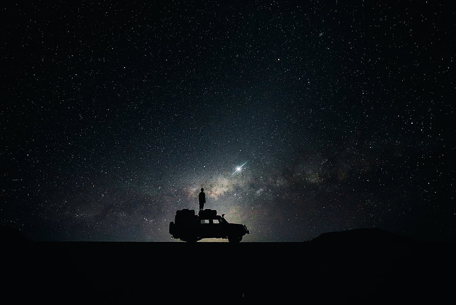 Silhouette of a person standing on a vehicle beneath the Milky Way galaxy and starry night sky HD wallpaper