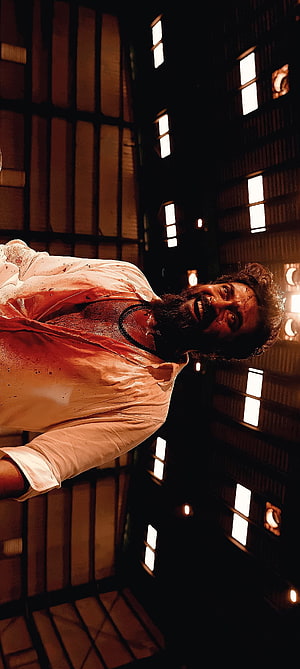 Suriya as Vikram in dramatic low-angle cinematic portrait with blood-stained shirt HD phone wallpaper