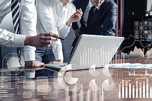 Business Team Analyzing Financial Data and Market Charts on Laptop in Modern Office HD wallpaper