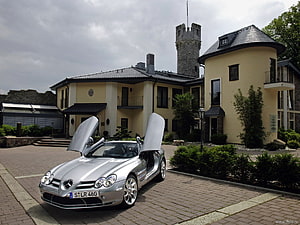 Silver Mercedes-Benz SLR McLaren with gullwing doors parked before a European castle estate HD wallpaper