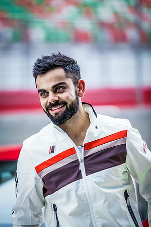 Virat Kohli smiling in a white and maroon sports jacket at a stadium HD phone wallpaper