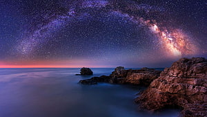 Milky Way Galaxy Arching Over a Rocky Coastal Shore at Night HD wallpaper