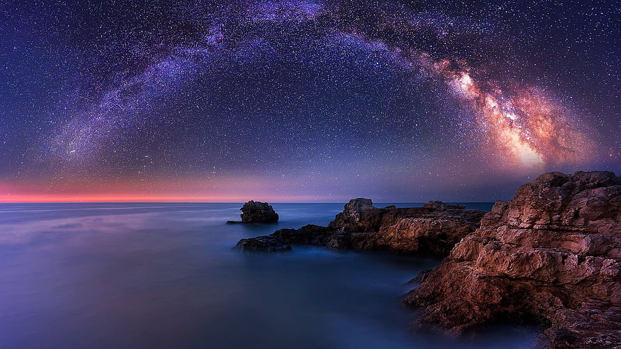 Milky Way Galaxy Arching Over a Rocky Coastal Shore at Night HD wallpaper