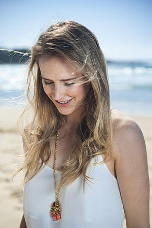 Ellyse Perry in a white dress on a sunny beach with windblown hair and a gold pendant necklace HD phone wallpaper