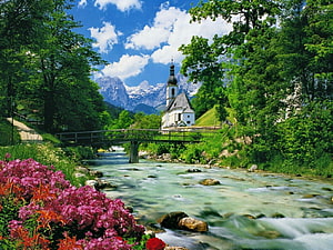 St. Bartholomew Chapel in the Bavarian Alps with a flowing river and vibrant summer flowers HD wallpaper