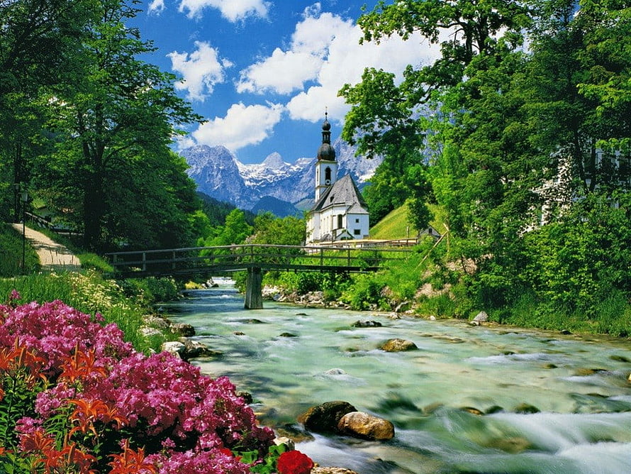 St. Bartholomew Chapel in the Bavarian Alps with a flowing river and vibrant summer flowers HD wallpaper