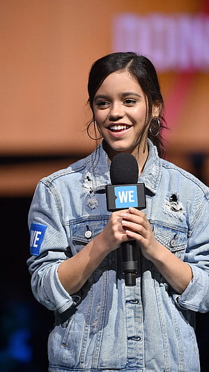 Jenna Ortega Smiling on Stage in Distressed Denim Jacket Holding Microphone HD phone wallpaper