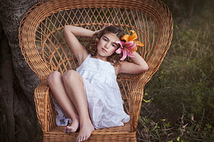 Young girl in white dress sitting in wicker chair with lily flowers outdoors HD wallpaper