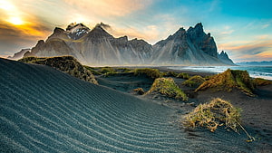 Dramatic Coastal Mountain Range Rising Above Black Sand Dunes at Golden Hour HD wallpaper