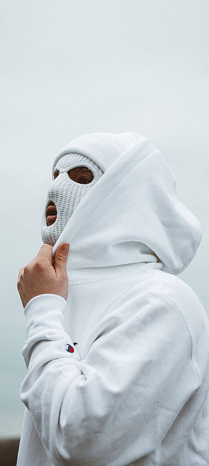 Person in white hoodie and knit face mask against a pale sky HD phone wallpaper
