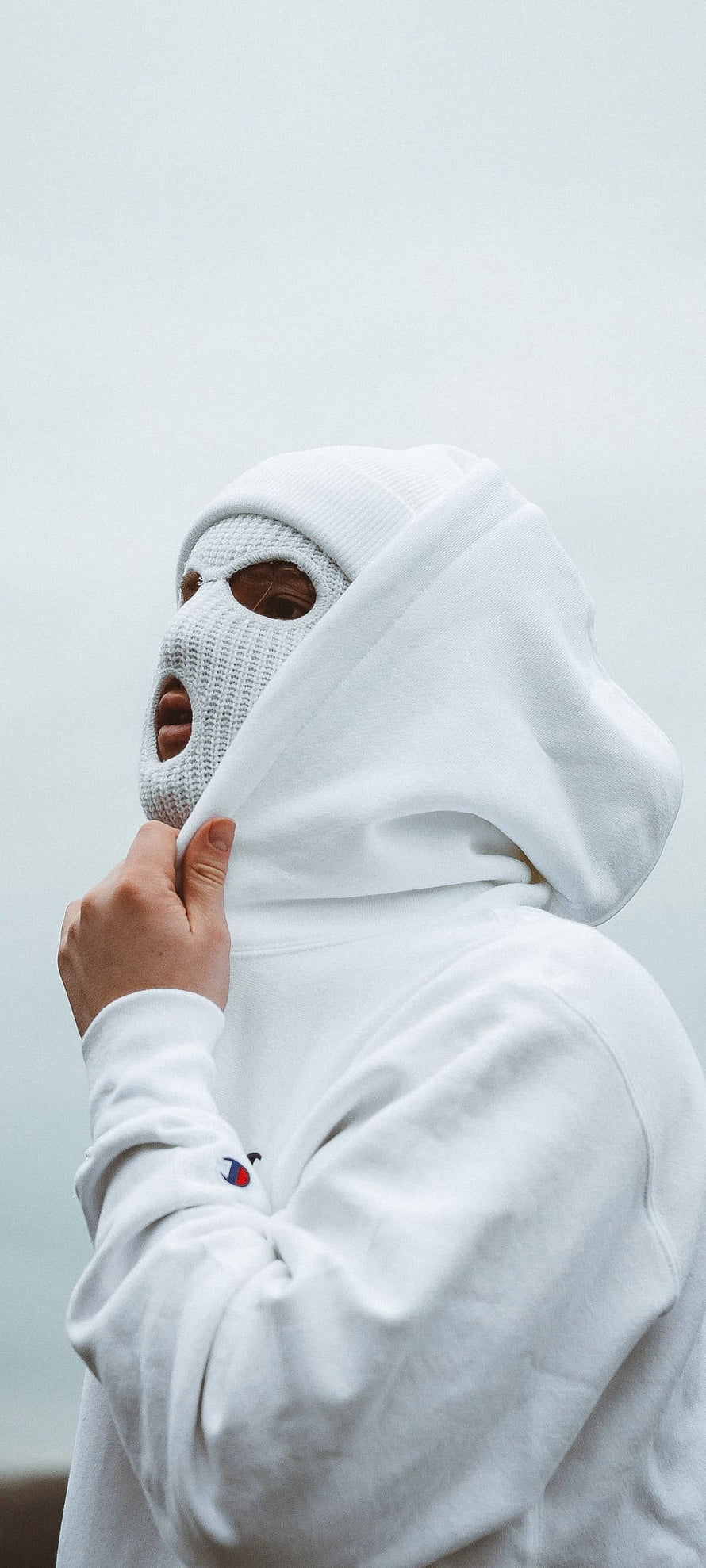 Person in white hoodie and knit face mask against a pale sky HD phone wallpaper
