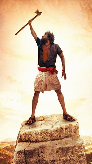 Pushpa Raj character standing on stone block holding raised axe in desert landscape HD phone wallpaper