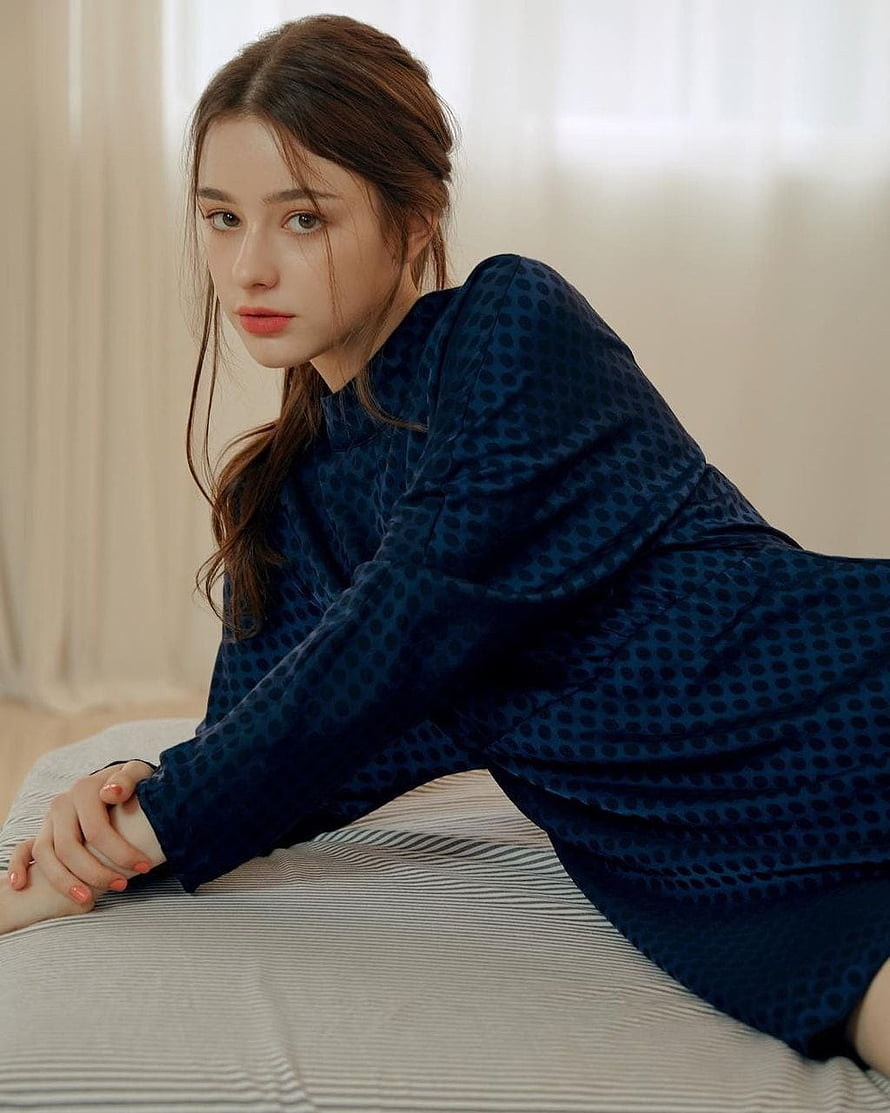 Dasha Taran in a navy blue polka dot dress reclining on a bed with soft natural lighting HD phone wallpaper