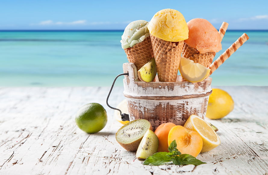 Colorful fruit ice cream cones in a rustic wooden bucket with fresh kiwi, lemon, and lime on a white beach table HD wallpaper