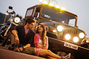 Sidharth Malhotra and a woman sitting in front of a vintage jeep and motorcycle at dusk HD wallpaper