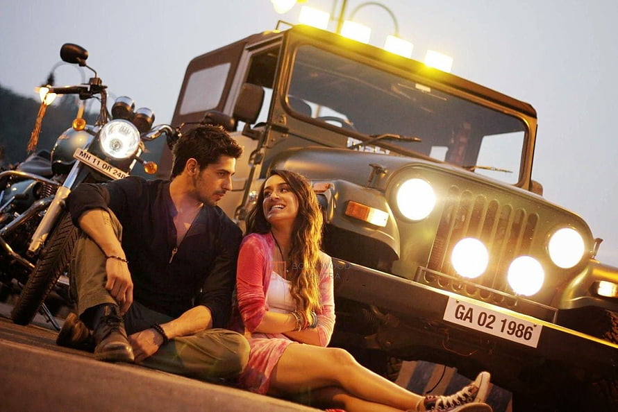 Sidharth Malhotra and a woman sitting in front of a vintage jeep and motorcycle at dusk HD wallpaper