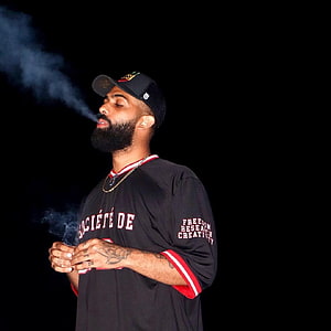 Eladio Carrión performing on stage in a black jersey with smoke effects HD phone wallpaper