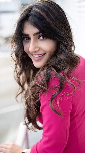 Sreeleela in a vibrant pink top with long wavy hair and a warm smile HD phone wallpaper
