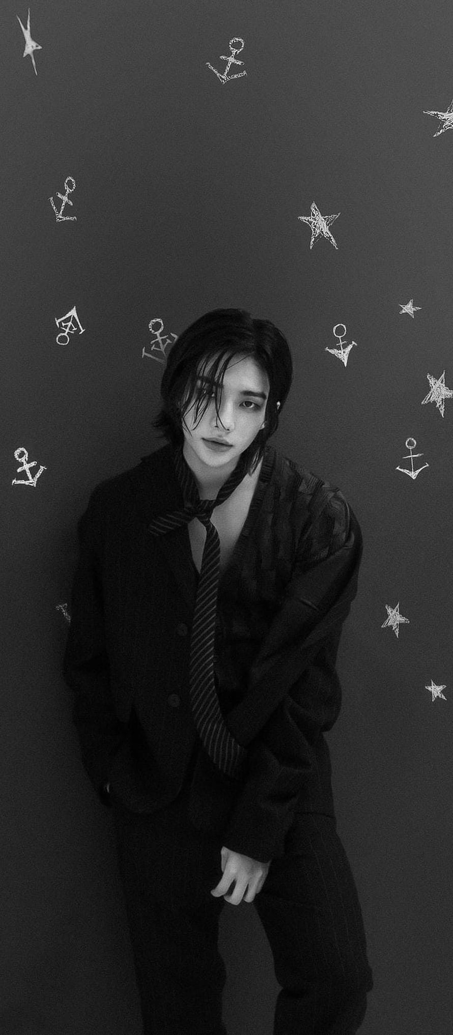 Hyunjin from Stray Kids in a black suit with a loose tie against a dark background with star and anchor doodles HD phone wallpaper