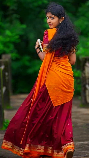 Young woman in a vibrant orange and maroon Kerala sari standing in a lush green garden HD phone wallpaper