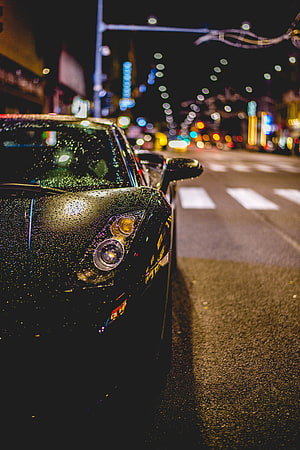 Black sports car with rain droplets parked on a city street at night with bokeh lights HD phone wallpaper