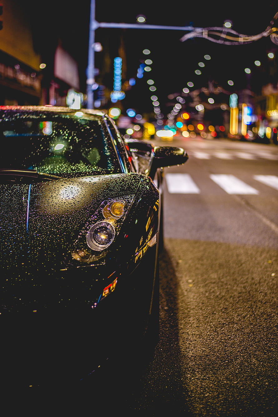 Black sports car with rain droplets parked on a city street at night with bokeh lights HD phone wallpaper