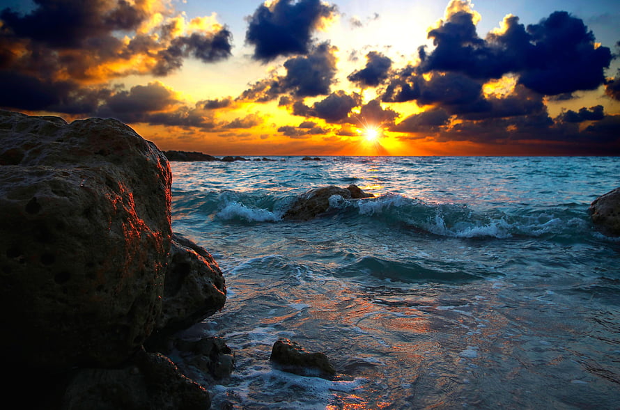 Golden sunset over a rocky coastline with crashing waves and dramatic clouds HD wallpaper