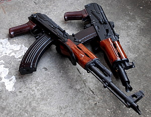 Two AK-47 assault rifles with wooden furniture resting on a concrete surface HD wallpaper