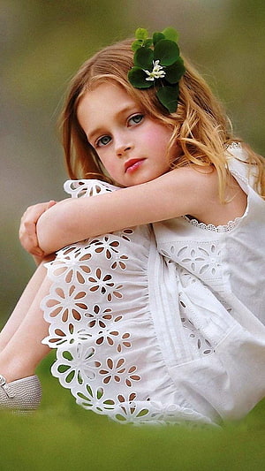 Young girl in white eyelet dress with green leaf hair accessory sitting in grass HD phone wallpaper