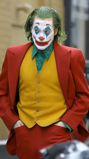 Joaquin Phoenix as The Joker in a red suit with green hair and clown makeup HD phone wallpaper