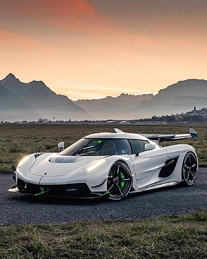 White Koenigsegg Jesko hypercar parked on gravel with mountain backdrop at sunset HD phone wallpaper