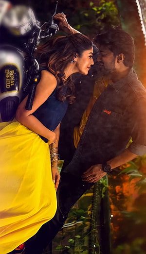 Vijay and Nayanthara romantic scene on a Royal Enfield motorcycle in a lush garden setting HD phone wallpaper