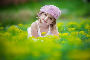 Smiling young girl in pink hat lying in a field of yellow wildflowers HD wallpaper