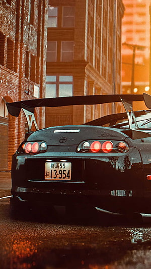 Rear View of a Black Toyota Supra with Large Rear Wing on a Wet City Street at Dusk HD phone wallpaper