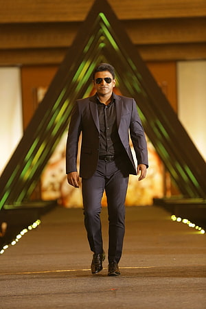 Punit Rajkumar in a dark suit and sunglasses walking on a runway with geometric green lighting HD phone wallpaper