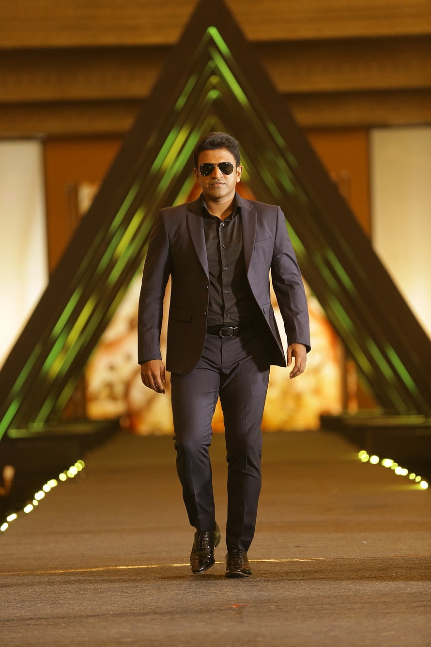Punit Rajkumar in a dark suit and sunglasses walking on a runway with geometric green lighting HD phone wallpaper